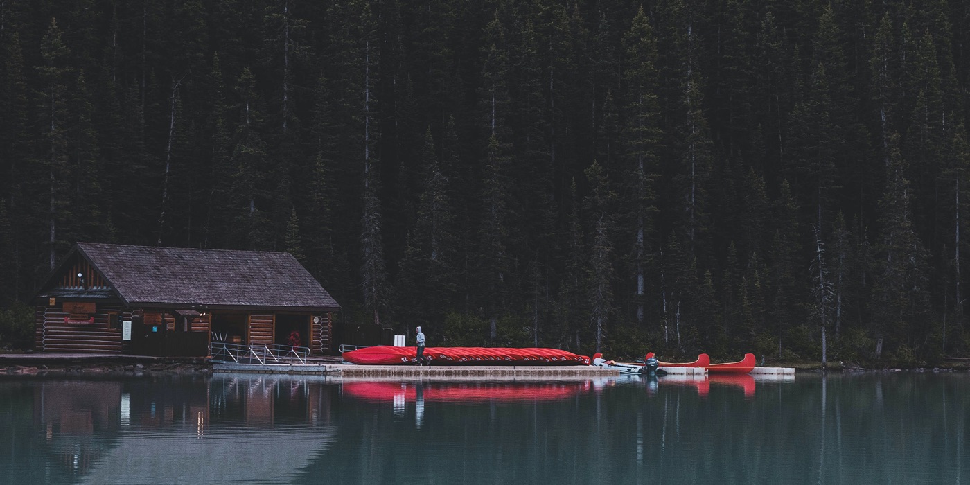Lakeside boathouse with red canoes beneath a forested mountainside in Alberta